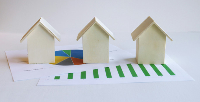 Three wooden house models sitting on a pieces of paper with charts and graphs on them.