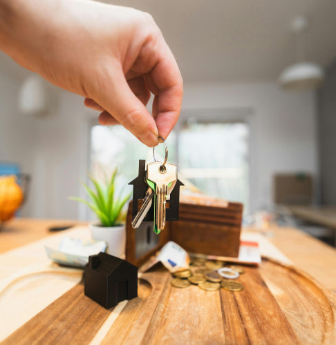 A hand holding a set of keys in front of a wallet with a modern home interior as the backdrop.